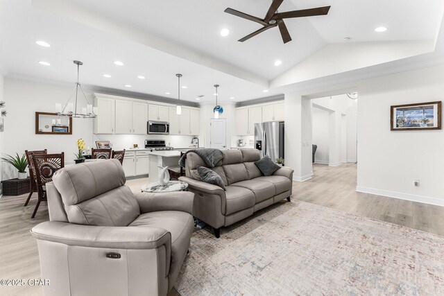 living room with ceiling fan with notable chandelier, vaulted ceiling, ornamental molding, and light hardwood / wood-style flooring