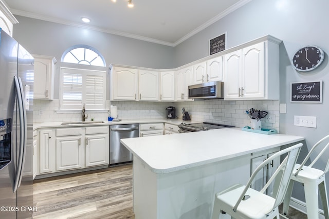 kitchen featuring light countertops, appliances with stainless steel finishes, white cabinets, a sink, and a peninsula