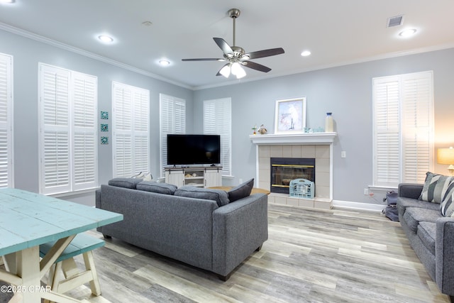 living room with light wood finished floors, visible vents, crown molding, and a tile fireplace