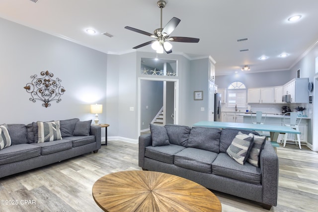 living area featuring light wood-type flooring, visible vents, and crown molding