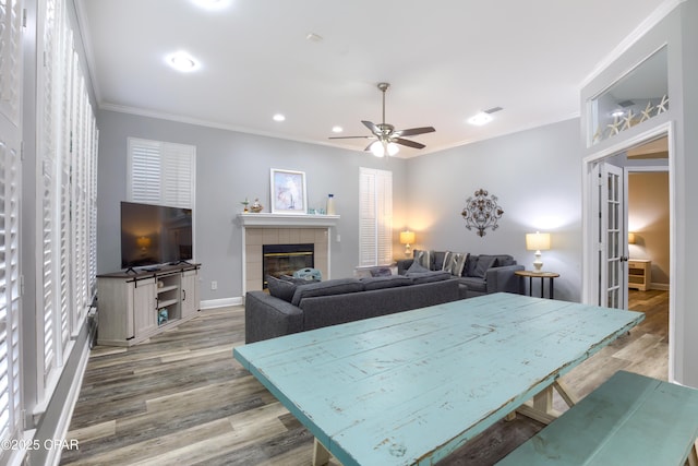 living room with crown molding, recessed lighting, wood finished floors, a tile fireplace, and baseboards