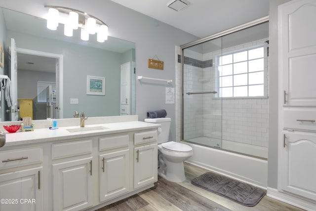 bathroom featuring enclosed tub / shower combo, toilet, wood finished floors, and vanity