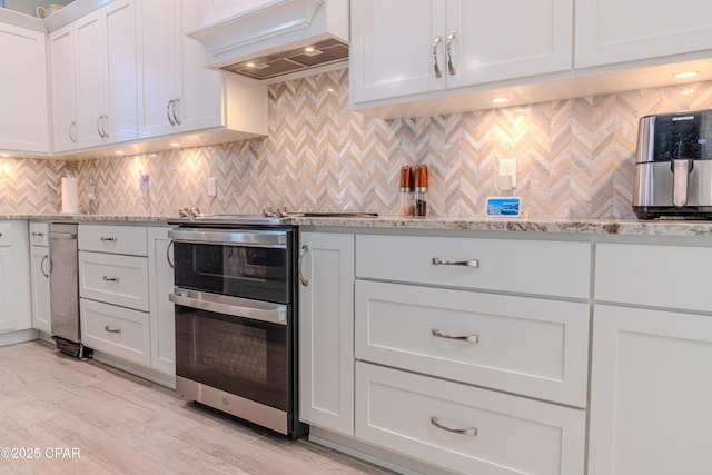 kitchen with tasteful backsplash, white cabinetry, range with two ovens, light stone counters, and custom range hood