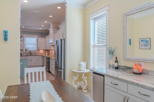 kitchen featuring sink, stainless steel refrigerator, light stone counters, white cabinets, and decorative backsplash