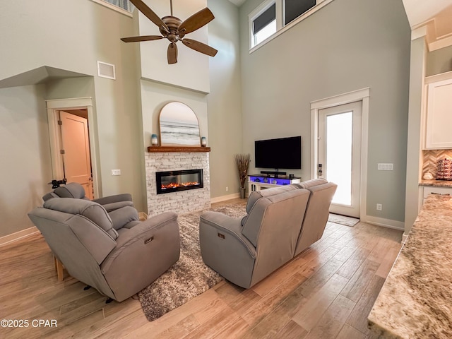 living room with ceiling fan, a healthy amount of sunlight, a fireplace, and a high ceiling