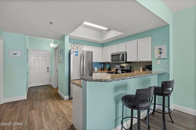 kitchen with white cabinetry, light hardwood / wood-style floors, kitchen peninsula, stainless steel appliances, and backsplash