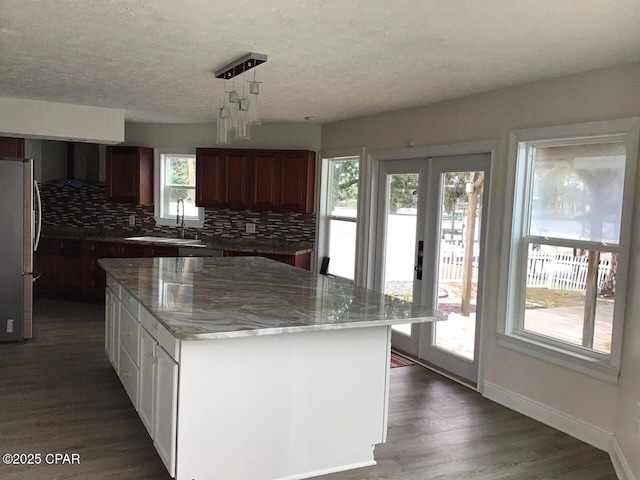 kitchen featuring decorative light fixtures, dark hardwood / wood-style floors, a kitchen island, sink, and stainless steel refrigerator