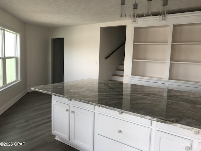 kitchen featuring a textured ceiling, dark wood-type flooring, white cabinetry, dark stone counters, and built in features