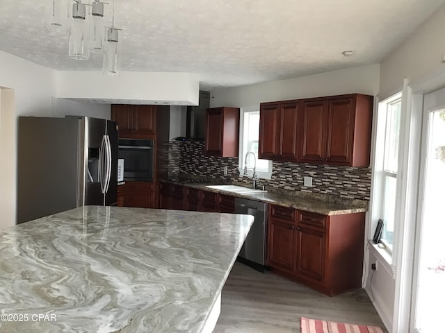 kitchen featuring backsplash, light wood-type flooring, wall chimney range hood, black appliances, and sink