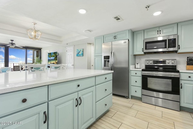 kitchen featuring ceiling fan, appliances with stainless steel finishes, decorative light fixtures, green cabinetry, and light stone counters