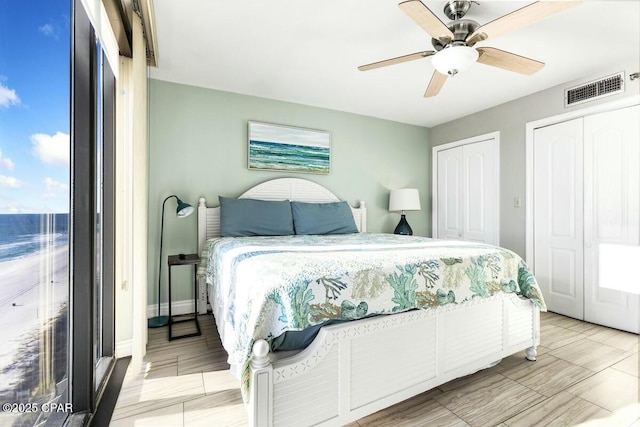 bedroom with ceiling fan, a water view, and multiple closets