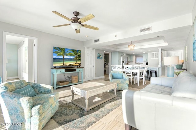 living room featuring ceiling fan with notable chandelier and a tray ceiling