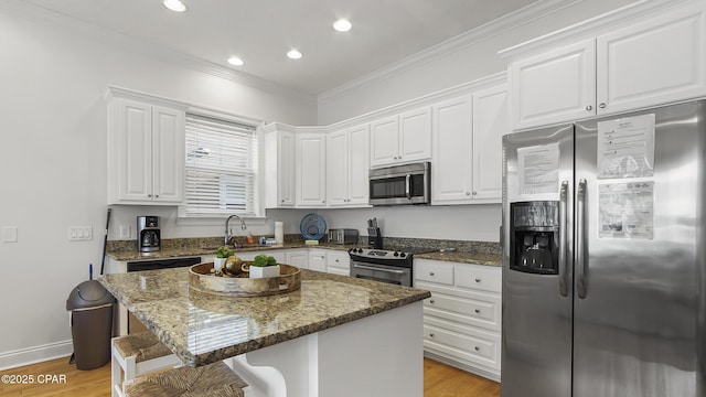 kitchen featuring white cabinetry, appliances with stainless steel finishes, a center island, and dark stone counters