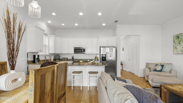 kitchen with crown molding, hanging light fixtures, stainless steel appliances, white cabinets, and dark stone counters