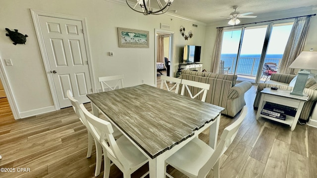 dining room with ceiling fan with notable chandelier, a textured ceiling, light hardwood / wood-style flooring, and crown molding