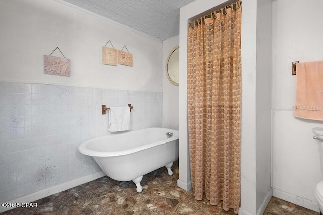 full bathroom featuring tile walls, a textured ceiling, a soaking tub, toilet, and wainscoting