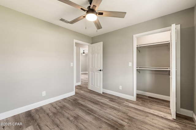 unfurnished bedroom with a closet, visible vents, a ceiling fan, wood finished floors, and baseboards