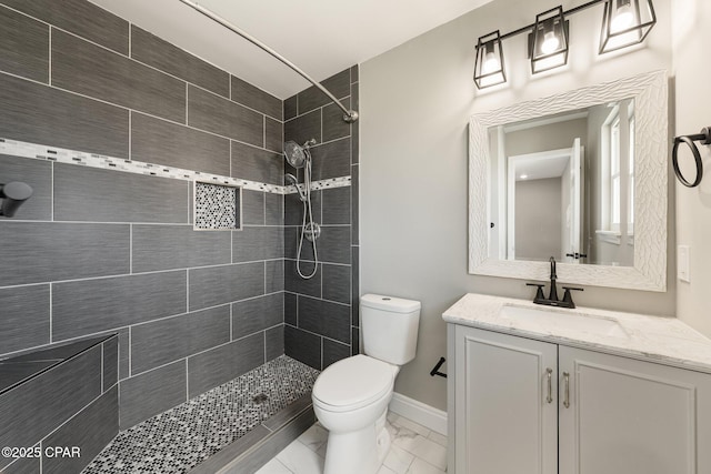 bathroom featuring marble finish floor, tiled shower, vanity, and toilet