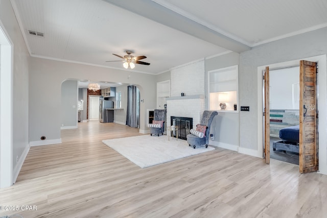 living room featuring a fireplace, ceiling fan, light wood-type flooring, and crown molding