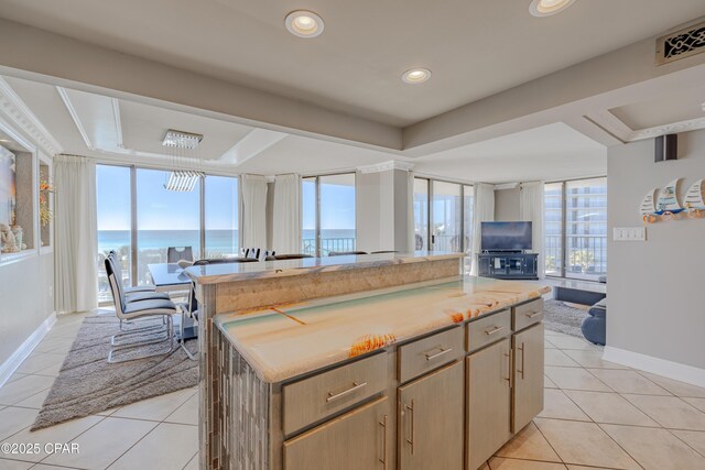 kitchen featuring a wall of windows, a water view, light brown cabinetry, a kitchen island, and light tile patterned flooring