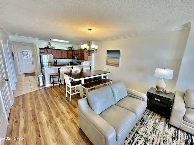 living room featuring crown molding, a textured ceiling, a notable chandelier, and light hardwood / wood-style flooring