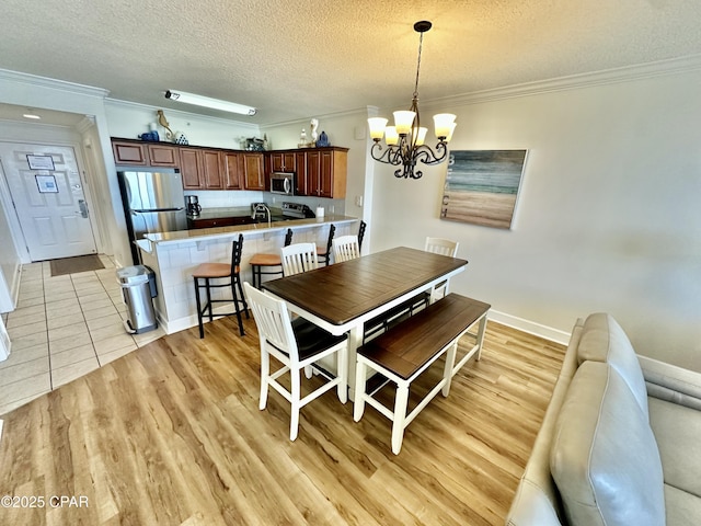 dining room with light wood-type flooring, a notable chandelier, a textured ceiling, and ornamental molding