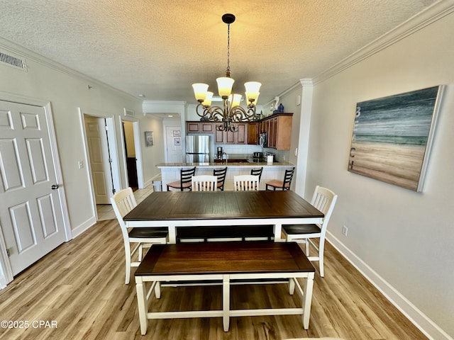 dining space with light hardwood / wood-style floors, a notable chandelier, a textured ceiling, and ornamental molding