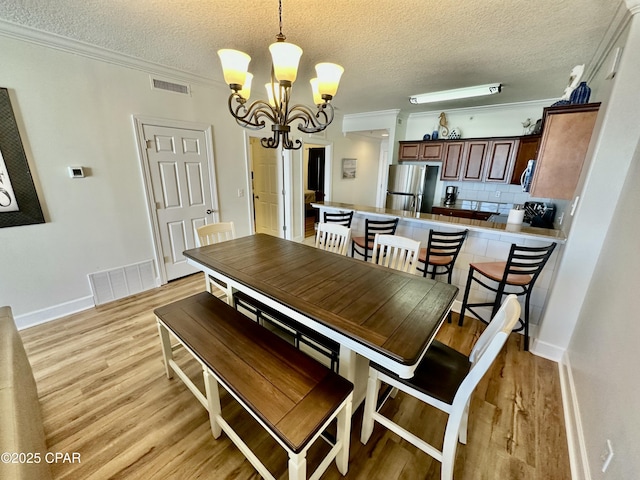 dining area featuring a textured ceiling, light wood-type flooring, crown molding, and an inviting chandelier