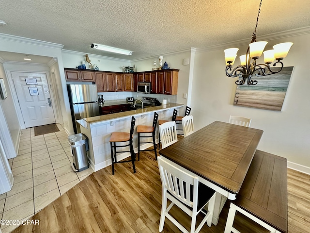 kitchen with kitchen peninsula, a kitchen bar, an inviting chandelier, appliances with stainless steel finishes, and a textured ceiling