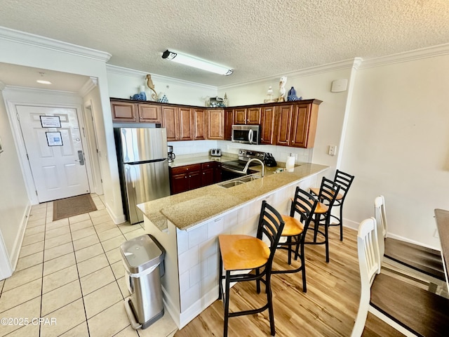 kitchen with kitchen peninsula, stainless steel appliances, tasteful backsplash, ornamental molding, and sink