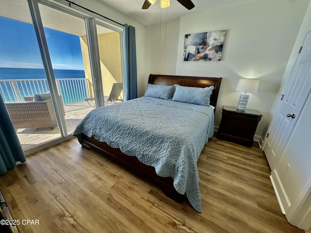 bedroom with access to outside, ceiling fan, hardwood / wood-style floors, and a water view