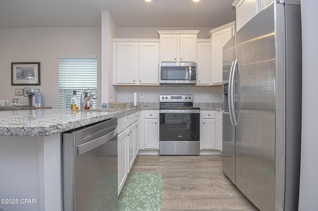 kitchen featuring light stone counters, appliances with stainless steel finishes, light wood-type flooring, and white cabinets