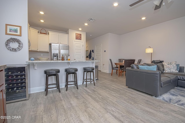 kitchen with a breakfast bar, light stone counters, light hardwood / wood-style flooring, ceiling fan, and stainless steel appliances