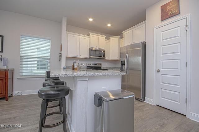 kitchen featuring light stone countertops, appliances with stainless steel finishes, white cabinets, and a kitchen breakfast bar