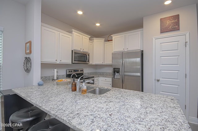 kitchen with a breakfast bar, sink, appliances with stainless steel finishes, kitchen peninsula, and white cabinets