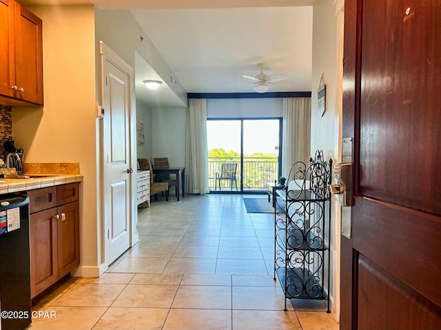 kitchen with sink, light tile patterned floors, tile counters, dishwashing machine, and ceiling fan