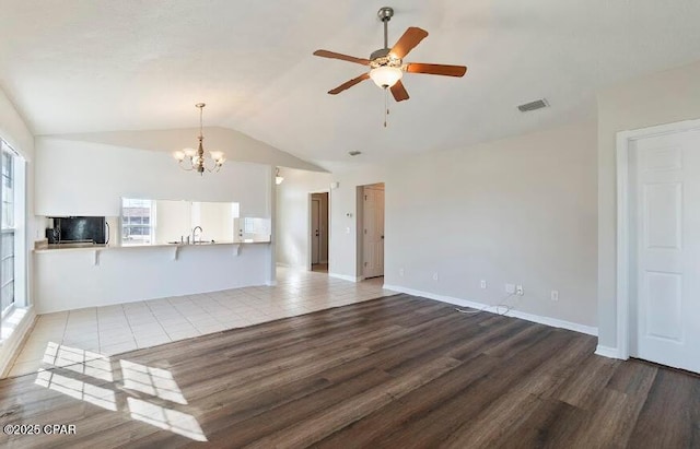 unfurnished living room with lofted ceiling, ceiling fan with notable chandelier, wood-type flooring, and sink