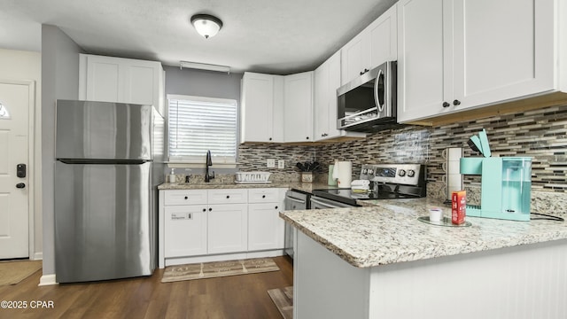 kitchen with kitchen peninsula, appliances with stainless steel finishes, light stone countertops, and white cabinetry