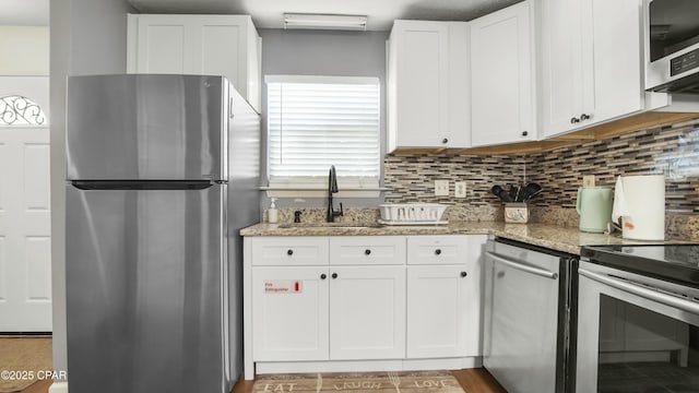 kitchen with stainless steel appliances, light stone countertops, tasteful backsplash, and white cabinetry