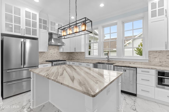 kitchen featuring appliances with stainless steel finishes, a center island, wall chimney exhaust hood, white cabinets, and sink