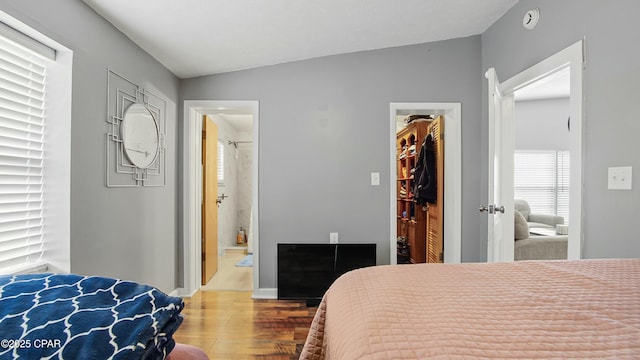 bedroom with a walk in closet, ensuite bath, lofted ceiling, a closet, and hardwood / wood-style flooring