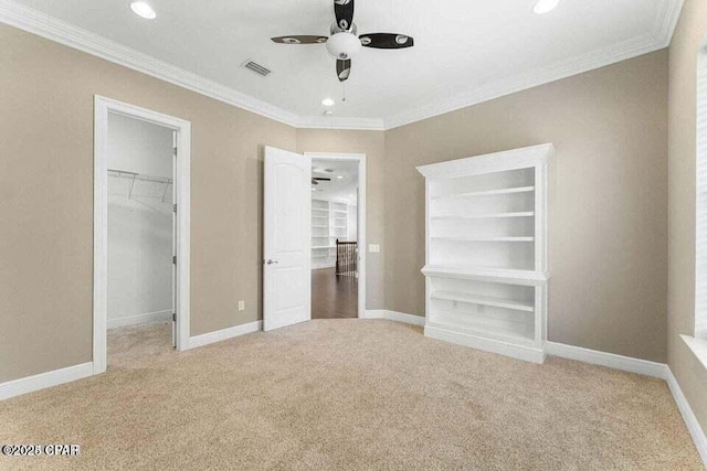 unfurnished bedroom featuring a spacious closet, a closet, carpet floors, crown molding, and ceiling fan