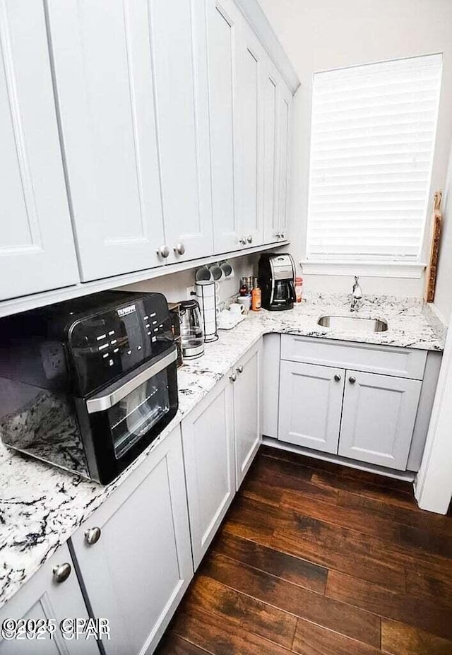 kitchen with white cabinets, dark hardwood / wood-style flooring, light stone counters, and sink