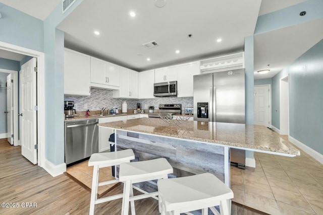 kitchen with stainless steel appliances, a kitchen island, white cabinets, and light stone countertops