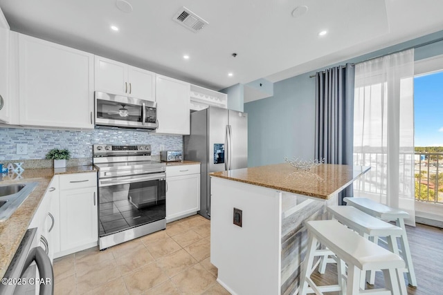 kitchen with appliances with stainless steel finishes, a center island, light stone countertops, white cabinets, and backsplash