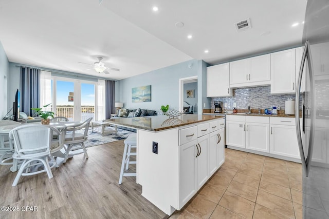 kitchen featuring a center island, stainless steel fridge, dark stone countertops, white cabinets, and ceiling fan