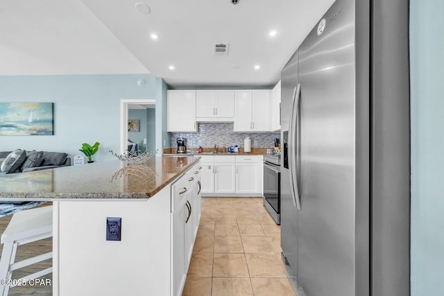 kitchen featuring stainless steel appliances, white cabinetry, a kitchen breakfast bar, dark stone counters, and a kitchen island