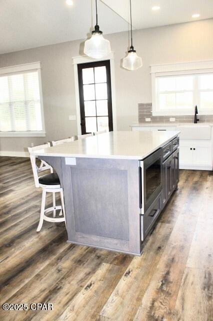 kitchen with stainless steel microwave, dark wood-type flooring, a center island, decorative light fixtures, and white cabinetry