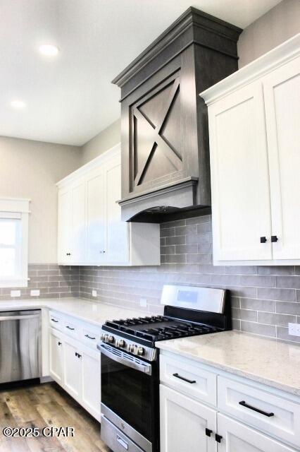 kitchen featuring hardwood / wood-style floors, stainless steel appliances, light stone counters, white cabinets, and backsplash