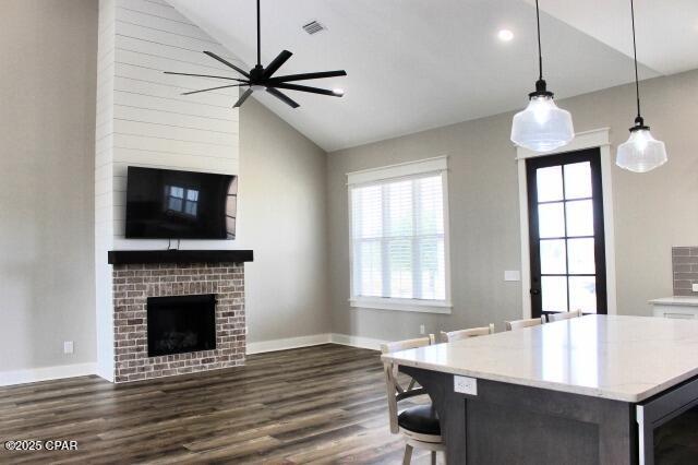 kitchen featuring vaulted ceiling, dark hardwood / wood-style floors, decorative light fixtures, a fireplace, and ceiling fan